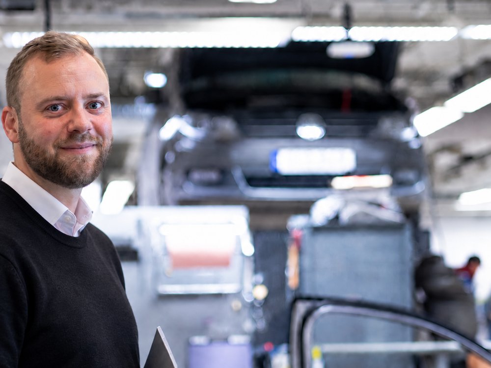 Medarbetare i verkstad med bil uppe på lyft i bakgrunden